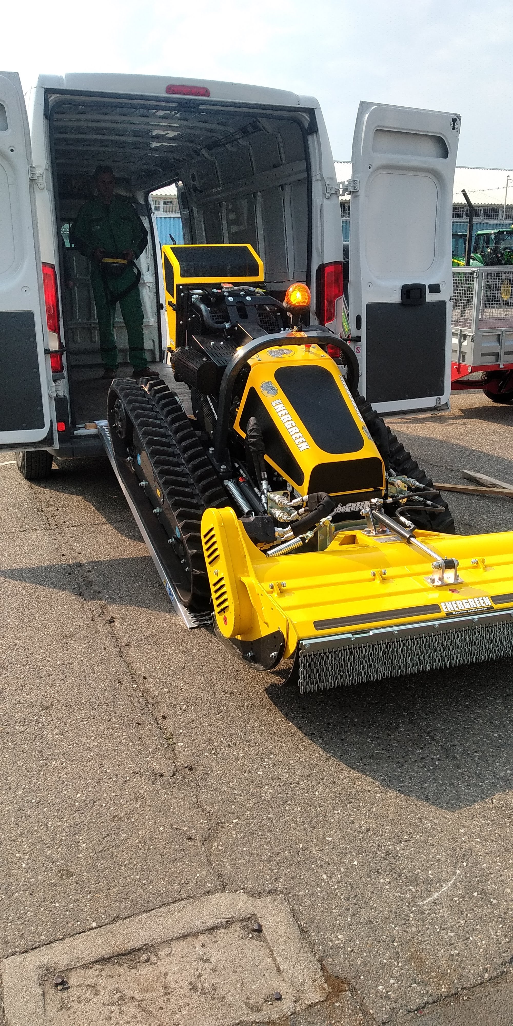 Yellow Energreen tracked mower or forestry mulcher being unloaded from white van on pavement.